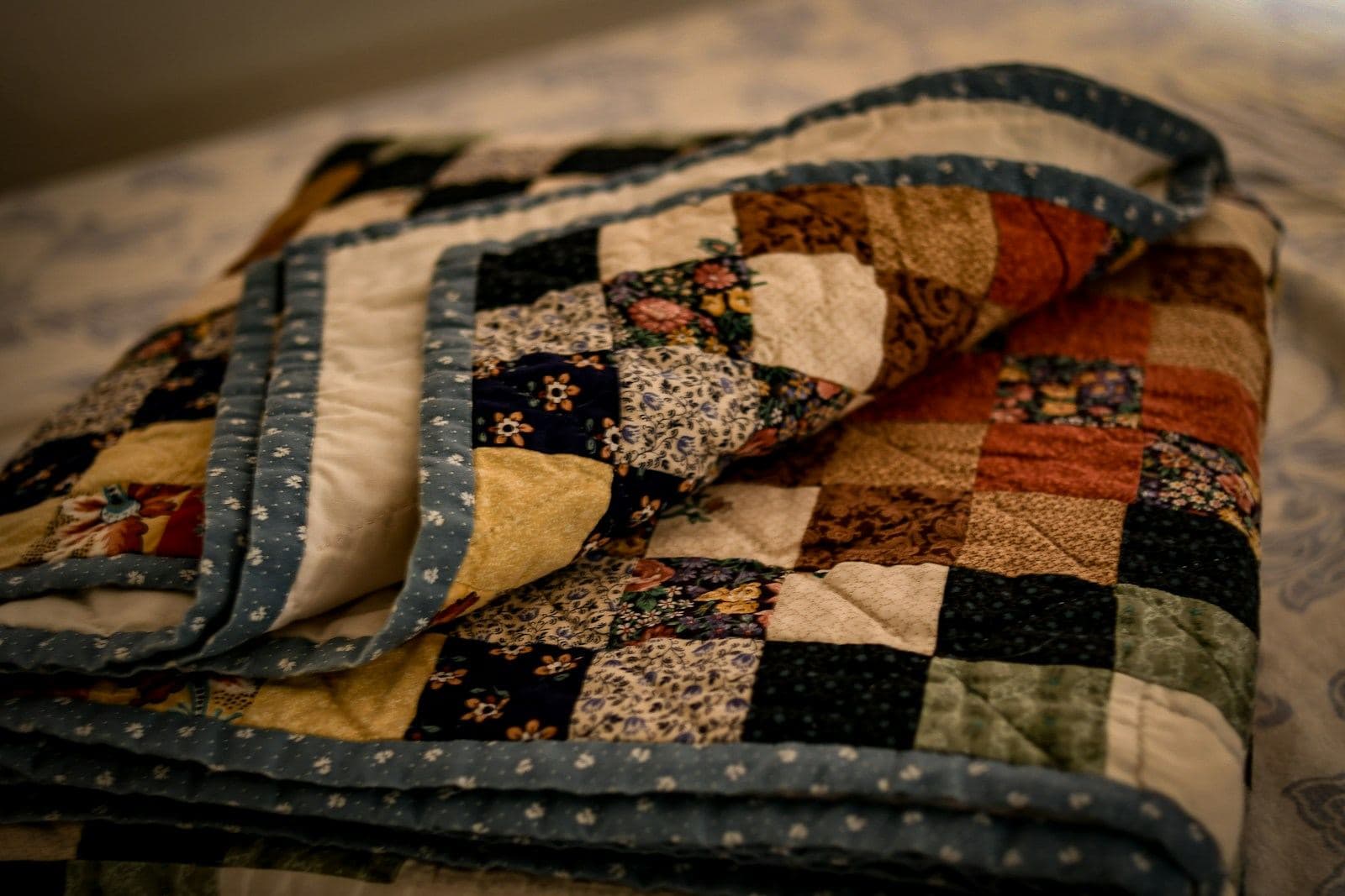 A folded patchwork quilt with a dark floral border