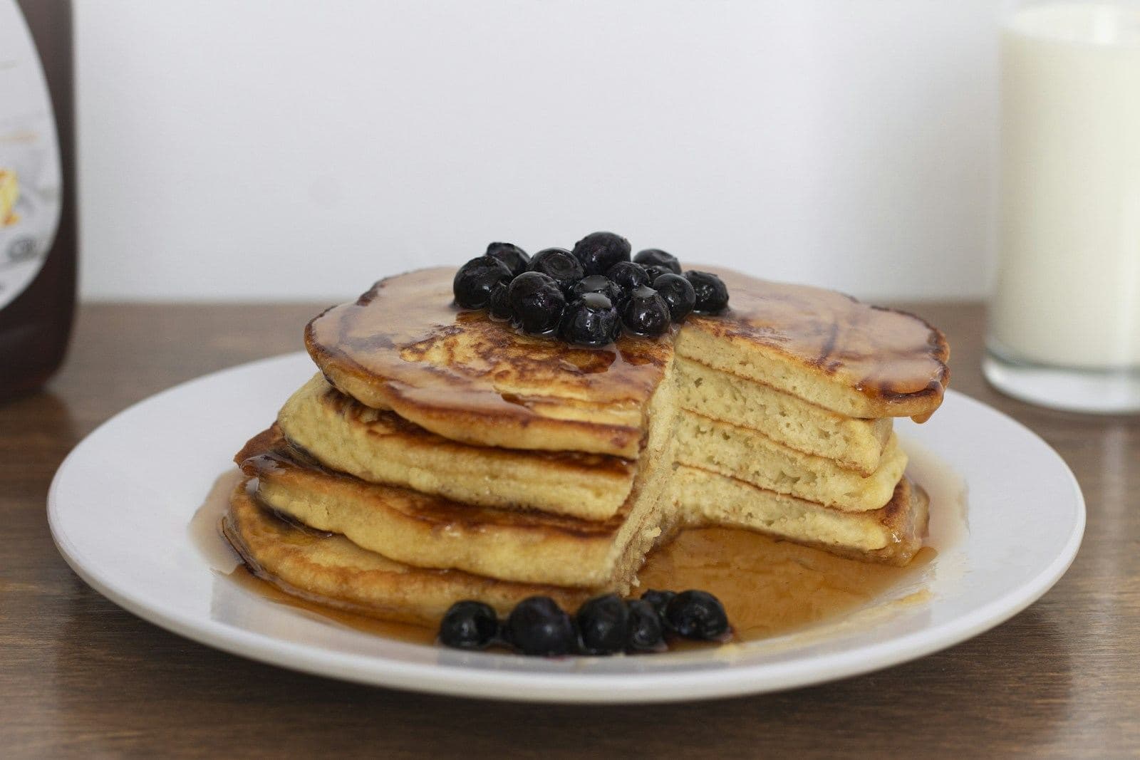 A stack of pancakes with syrup and blueberries on a white plate