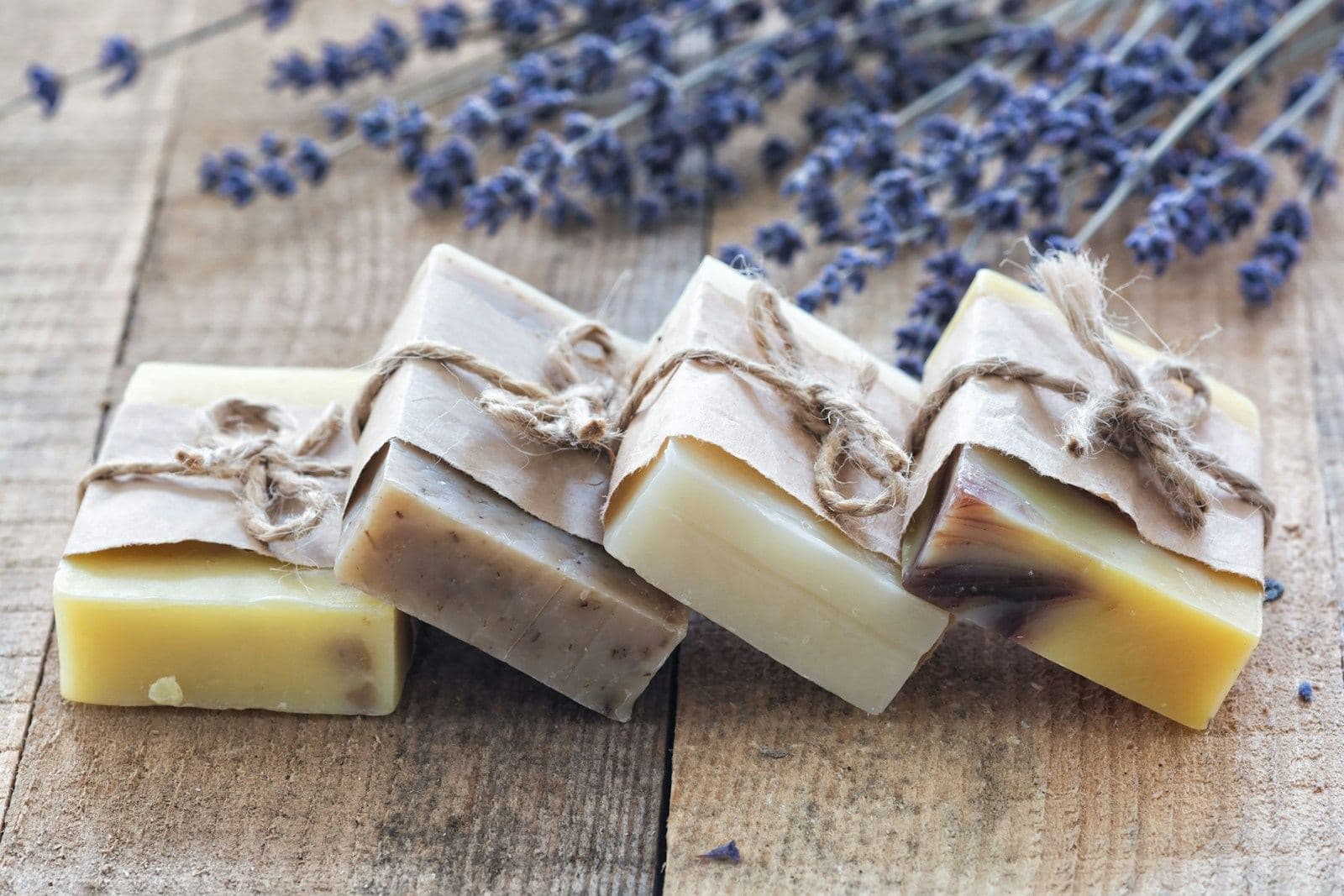 Four bars of handmade soap tied with twine beside dried lavender on a wooden table