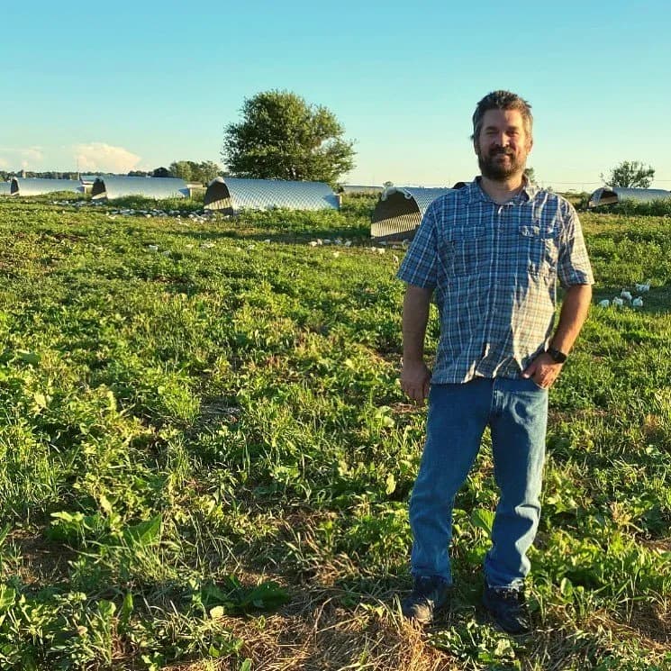 Greg Gunthorp standing in a pasture with poultry shelters behind him