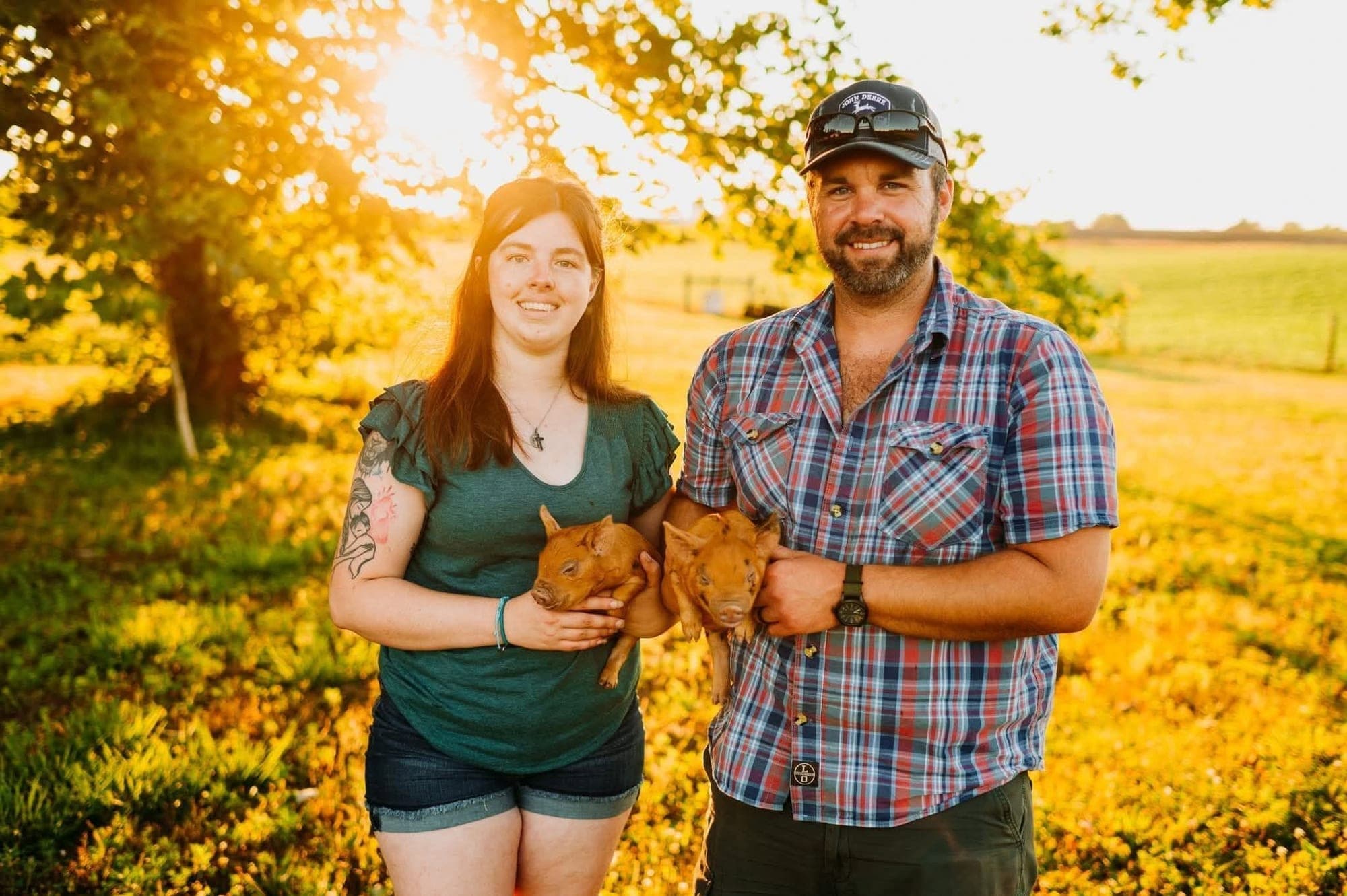 Tyler and Jessica Bowman holding two piglets in a sunny pasture